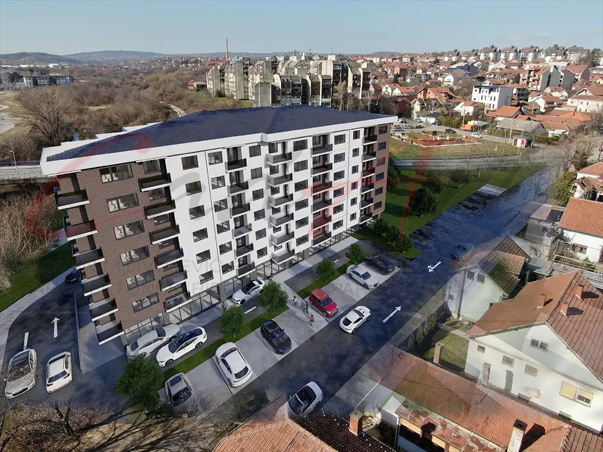 Photomontage of the design for a seven-story apartment building in Kragujevac, Serbia, set into a photograph of its site: aerial view with parking along the street.